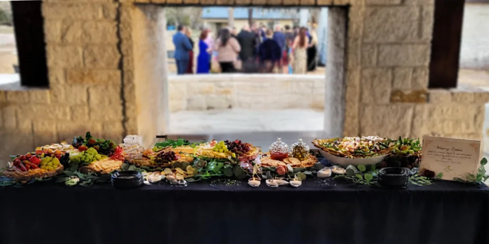Mana Sabroso grazing table beneath a stone pavilion, with guests gathered in the background