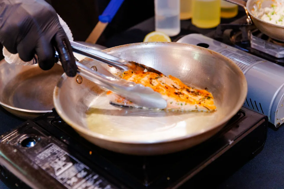 A chef cooking salmon in a pan on site
