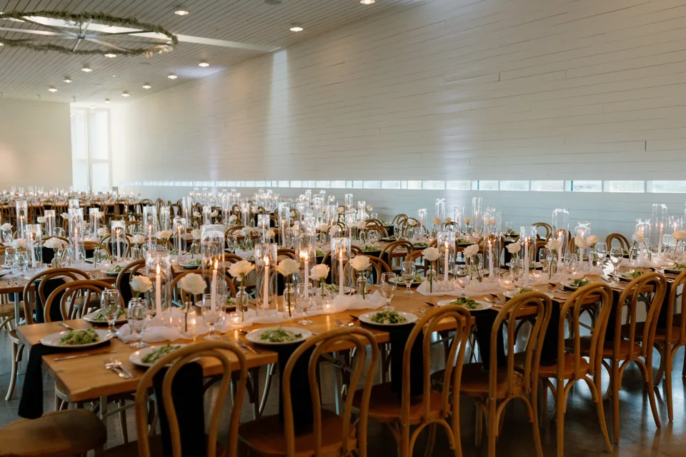 A wedding reception room with long tables, candles and wooden chairs