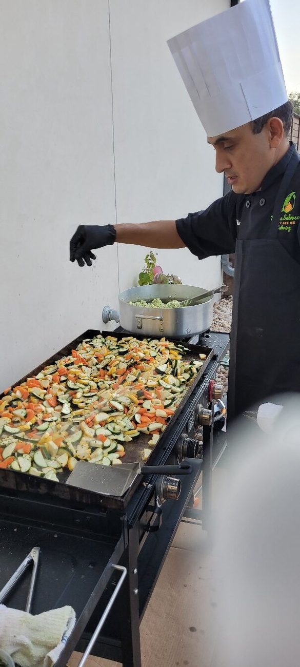 Chef Javier cooking at an outdoor flat-top griddle, seasoning fresh vegetables.