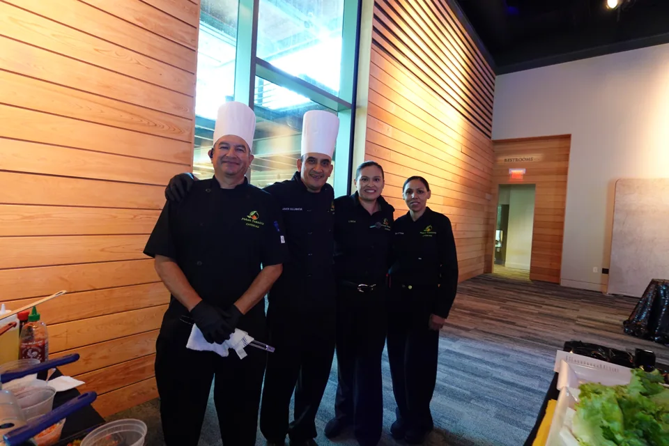 Four Mana Sabroso team members in uniform beside an event service table