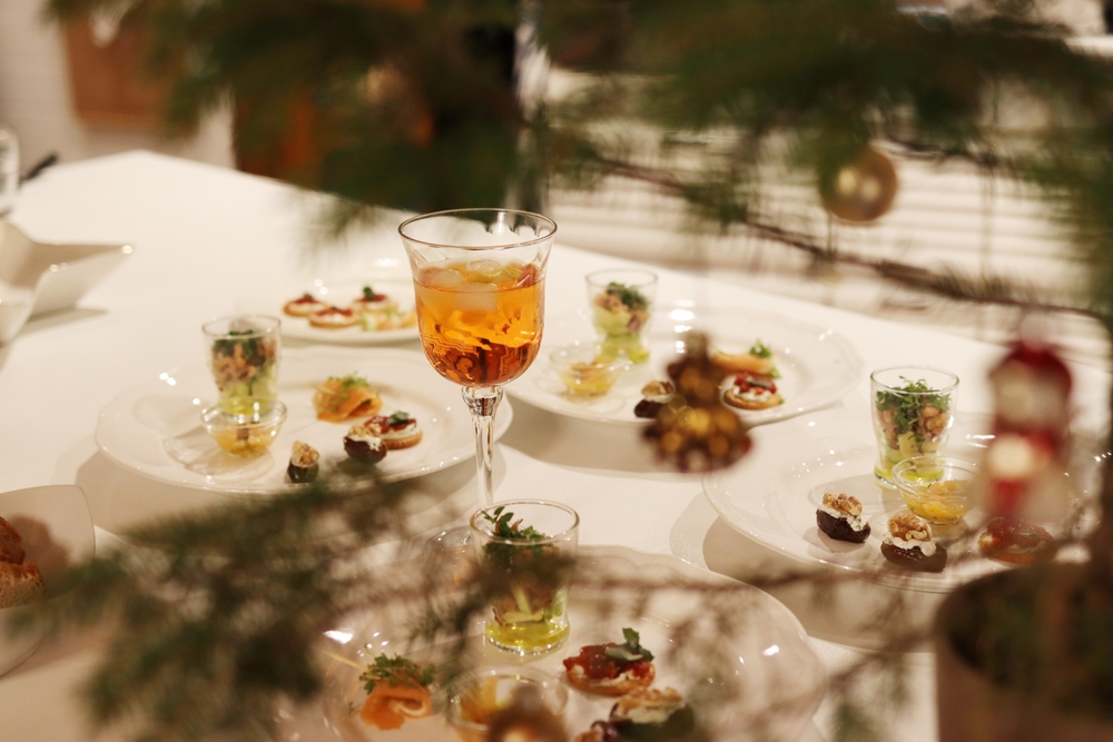 A table with a white tablecloth covered in plates with small, delicate foods and a glass of amber liquid