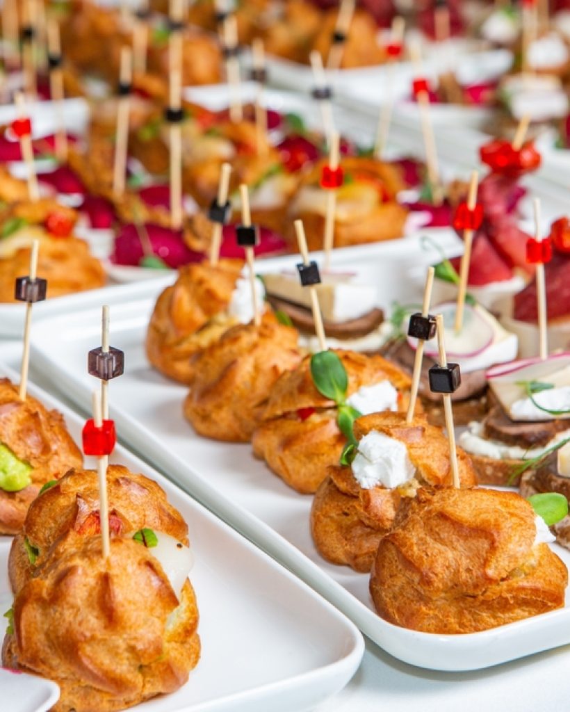 A collection of serving plates covered with rows of bite-sized foods with long toothpicks skewering them